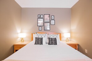 A neatly made bed with a wooden headboard, two bedside lamps, and a wall with framed pictures. - Complex hot tub | Close to Lifts | Free Parking (Whistler)
