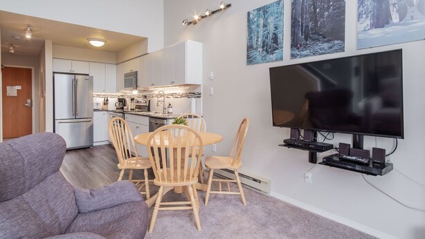 Een moderne woonkamer met een televisie, houten stoelen, een bank en een keuken op de achtergrond.
