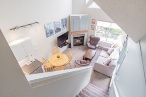 A modern living room with a fireplace, a dining area, and a staircase leading to an upper level. - Family friendly | Walk to Blackcomb | Hot tub (Whistler)