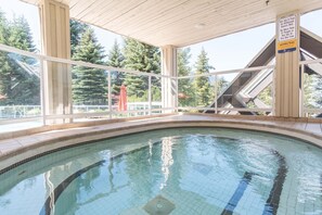 Ein hallenbad mit gefliestem Beckenrand, umgeben von einer Holzdielung und großen Fenstern.