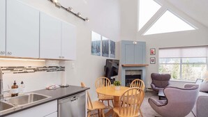 Een moderne keuken met een vaatwasser, een eethoek met een houten tafel en stoelen, een flatscreen-tv en een open haard.