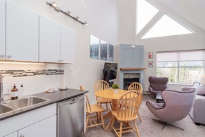 Eine moderne Küche mit Geschirrspüler, ein Essbereich mit Holztisch und Stühlen, einem Flachbildfernseher und einem Kamin.