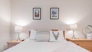 Een net opgemaakt bed met een witte dekbedovertrek en gestreepte kussens, met aan weerszijden nachtkastjes met lampen en een ringlamp.
