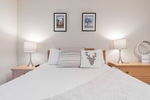 Ein ordentlich bezogenes Bett mit weißer Decke und gemusterten Kissen, an beiden Seiten zwei Nachttische mit Lampen und einem Ringlicht.