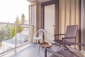 En balkong med en glasdörr, två stolar, ett litet bord och utsikt över träd och en byggnad.