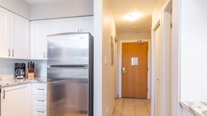 Una cocina con gabinetes blancos, un refrigerador de acero inoxidable, una cafetera y un bloque de cuchillos.