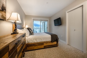 A bedroom with a bed, a wooden dresser, a lamp, a television, and a window with a view. - Renovated 1BDR + Loft | Just minutes from Lifts | Walk to everything (Whistler)