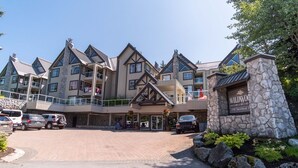 A multi-story lodge with a stone facade, balconies, and a parking area. - Short walk to Blackcomb | Free parking | Hot tub (Whistler)