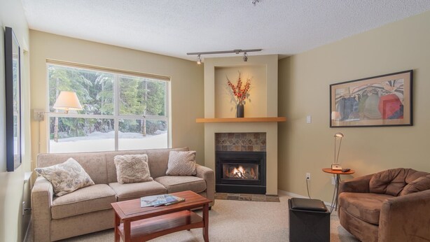A living room with a beige sofa, a wooden coffee table, a fireplace, and a painting on the wall. - Short walk to Blackcomb | Free parking | Hot tub (Whistler)