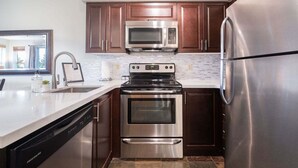 A compact kitchen with stainless steel appliances, wooden cabinets, and a window providing natural light. - Comfortable 2 Bdrm | Hot tub in complex | 5 min to Blackcomb (Whistler)