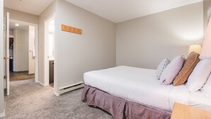 A bedroom with a bed, a wooden coat rack, a bedside table, and a lamp. - Comfortable 2 Bdrm | Hot tub in complex | 5 min to Blackcomb (Whistler)