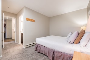 Ein Schlafzimmer mit einem Bett, einem Holz-Kleiderständer, einem Nachttisch und einer Lampe.