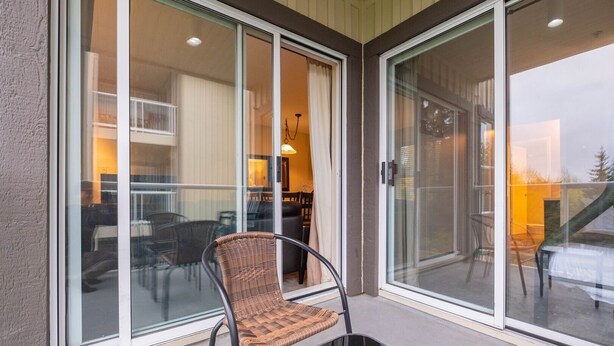 A balcony with a wicker chair, glass sliding doors, and a view of the interior. - Comfortable 2 Bdrm | Hot tub in complex | 5 min to Blackcomb (Whistler)