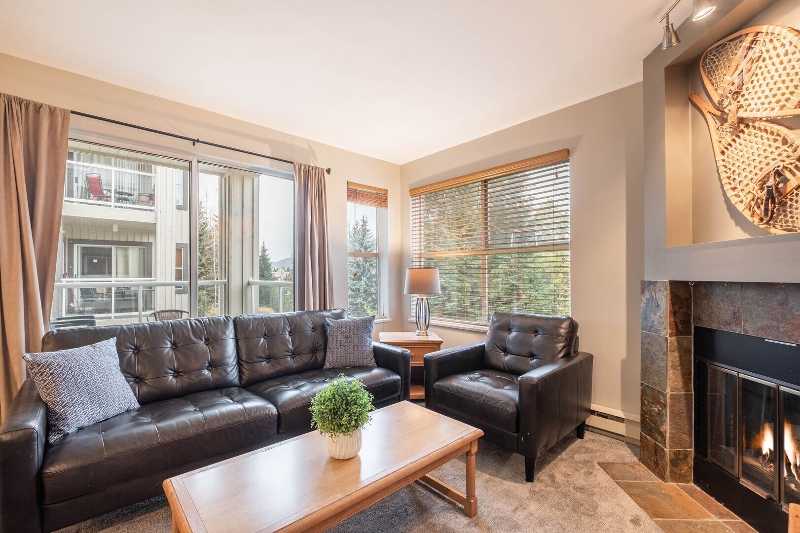 A living room with a leather sofa, a coffee table, a fireplace, and large windows.