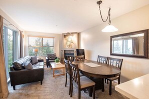 A living room with a fireplace, a dining table, and a sofa. - Comfortable 2 Bdrm | Hot tub in complex | 5 min to Blackcomb (Whistler)
