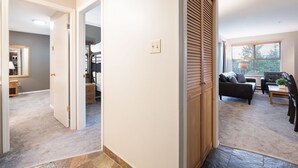 A hallway leading to a bedroom with a bunk bed, a living room with a sofa and a coffee table, and a window with blinds. - Comfortable 2 Bdrm | Hot tub in complex | 5 min to Blackcomb (Whistler)