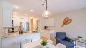 A modern kitchen with white cabinets, a marble countertop, and a dining area with a table and chairs. - Newly renovated 1 bedroom near Blackcomb Gondola - less than 5 min walk (Whistler)