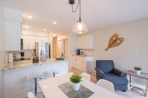 Una cocina moderna con armarios blancos, encimera de mármol y zona de comedor con mesa y sillas.