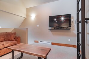 A modern living room with a flat-screen TV mounted on the wall, a wooden bench, and a brown sofa. - Large groups and families | Free parking | Hot tub (Whistler)