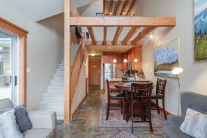 A modern kitchen with wooden beams, a dining area with a round table, and a staircase leading to an upper level. - Large groups and families | Free parking | Hot tub (Whistler)