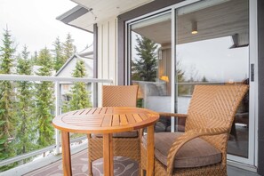 A balcony with a round wooden table and wicker chairs, overlooking a residential area with trees. - Large groups and families | Free parking | Hot tub (Whistler)