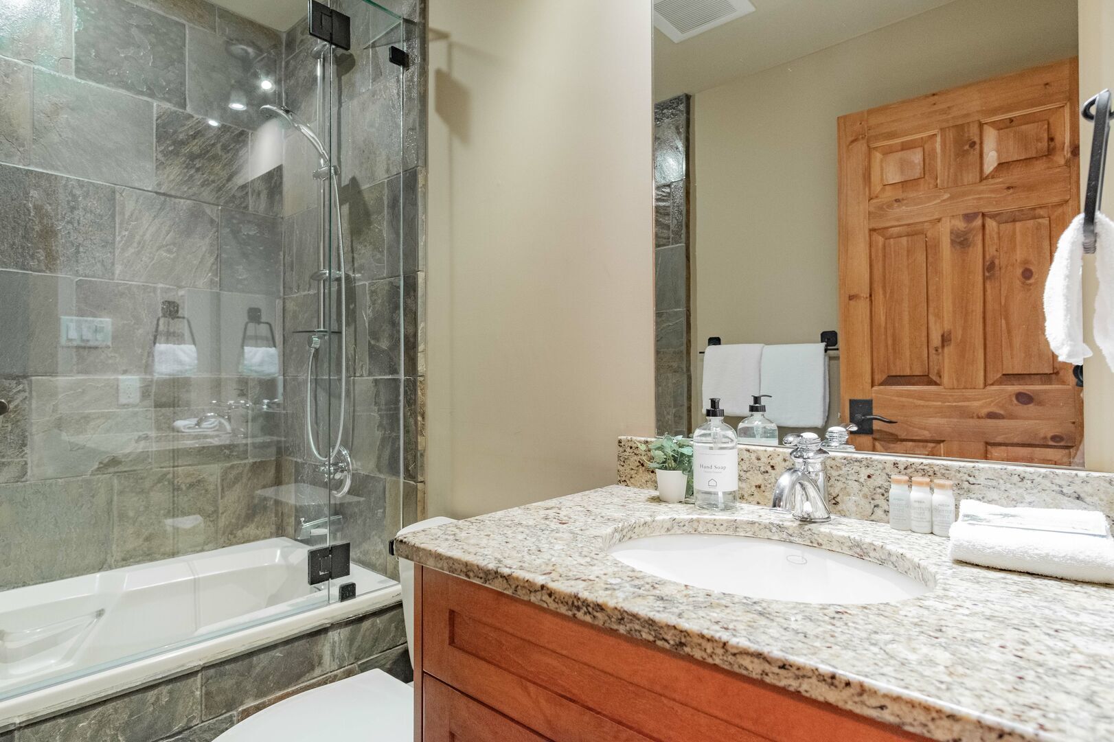 A bathroom with a glass-enclosed shower, a granite countertop, and wooden cabinets.