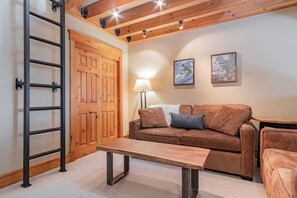 Une pièce avec un plafond en bois, une porte en bois, un canapé, une table et deux tableaux encadrés accrochés au mur.