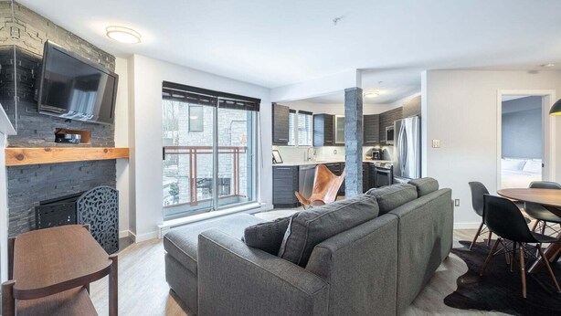 Ein modernes Wohnzimmer mit einem großen grauen Sofa, einem Kamin und einem Essbereich mit rundem Tisch und Stühlen.