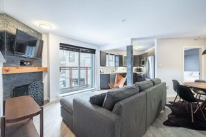 A modern living room with a large grey sofa, a fireplace, and a dining area with a round table and chairs. - AC in bedrooms | Village Centre | Pets (Whistler)