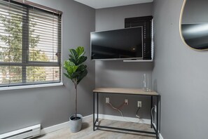 Een kamer met een groot raam, een wandtelevisie, een plant en een houten console.