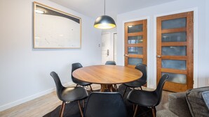Ein Essbereich mit einem runden Holztisch, schwarzen Stühlen, einer Pendelleuchte und zwei Holztüren mit Glasscheiben.