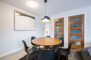 Ein Essbereich mit einem runden Holztisch, schwarzen Stühlen, einer Pendelleuchte und zwei Holztüren mit Glasscheiben.