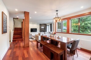 A modern living room with a wooden dining table, a sofa, and a TV mounted on the wall. - Spacious 2BDR on Blueberry Hill | Pets | Complex Hot Tub | BBQ (Whistler)