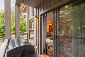 A covered outdoor area with a grill, sliding glass doors leading to a cozy interior with a sofa and a basket. - Spacious 2BDR on Blueberry Hill | Pets | Complex Hot Tub | BBQ (Whistler)