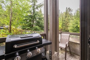 A balcony with a grill, a chair, and a view of trees. - Spacious 2BDR on Blueberry Hill | Pets | Complex Hot Tub | BBQ (Whistler)