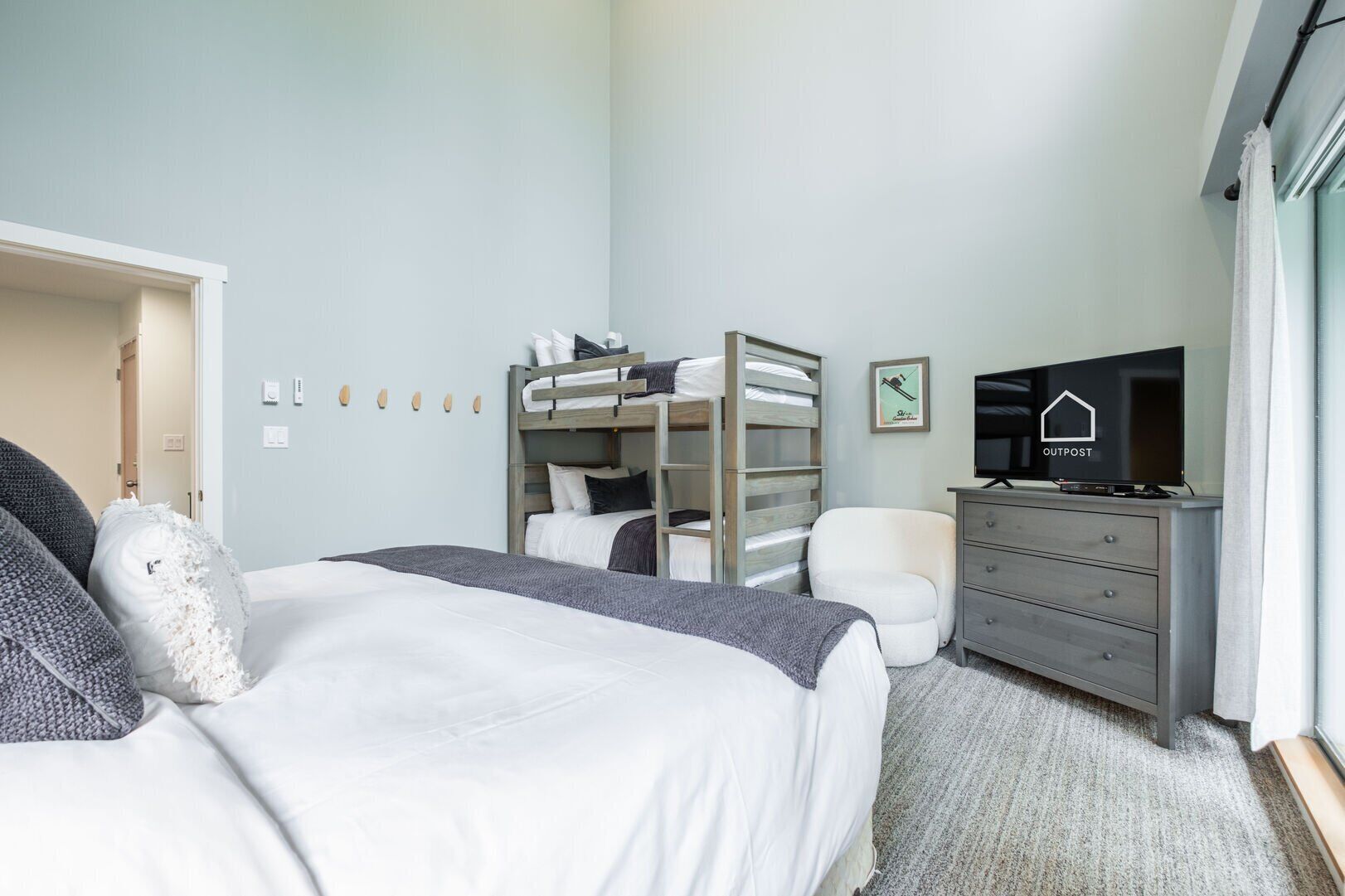 A bedroom with a bunk bed, a television, a dresser, and a door leading to another room.
