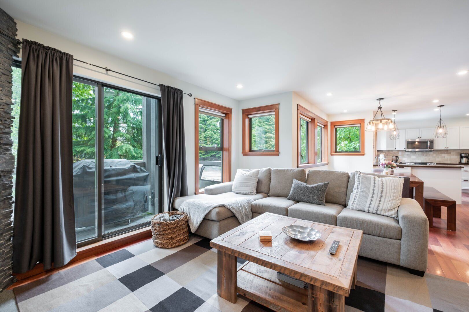A modern living room with a sofa, a wooden coffee table, and a kitchen in the background.