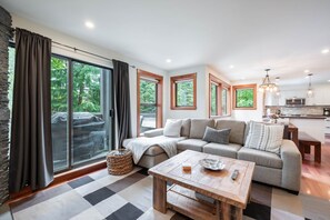 A modern living room with a sofa, a wooden coffee table, and a kitchen in the background. - Spacious 2BDR on Blueberry Hill | Pets | Complex Hot Tub | BBQ (Whistler)