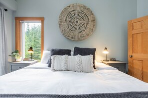 A bedroom with a large bed, two bedside tables with lamps, a round wall decoration, and a window with curtains. - Spacious 2BDR on Blueberry Hill | Pets | Complex Hot Tub | BBQ (Whistler)