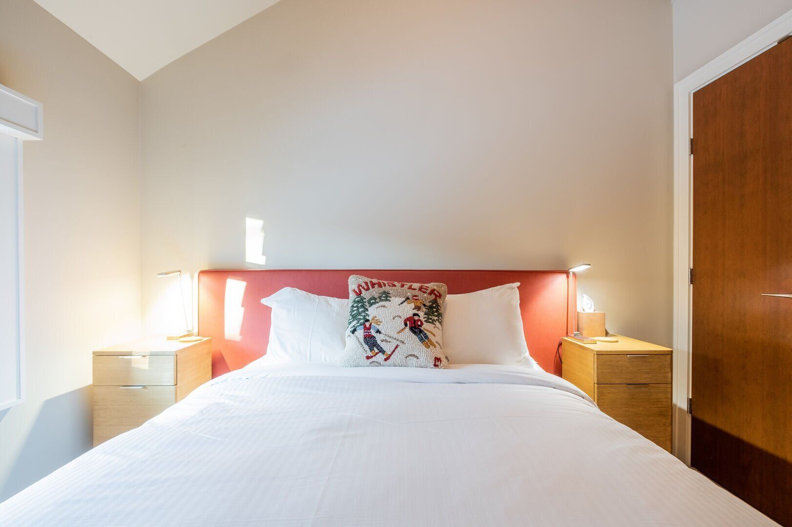 A neatly made bed with white linens, a red headboard, and a decorative pillow. There are two bedside tables with lamps.