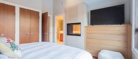 Un dormitorio con cama, televisor, armario de madera y baño visible a través de una puerta abierta.