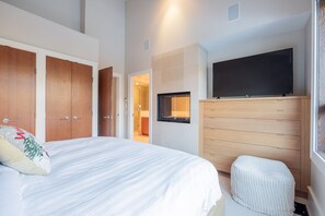 Quarto com cama, televisão, guarda-roupa de madeira e banheiro visível por uma porta aberta.