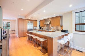 A modern kitchen with a large island, bar stools, and a view of the outdoors. - Luxury | AC | Private Hot Tub | BBQ | Pet friendly (Whistler)
