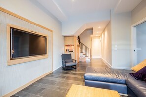 Ein modernes Wohnzimmer mit einem großen Flachbildfernseher, einer Couch, einem Sessel und einer Treppe, die zu einer anderen Ebene führt.