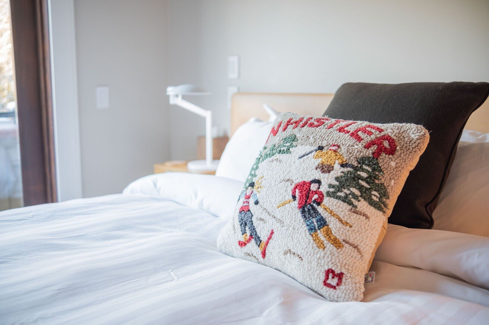 A bed with white bedding, a pillow with a Christmas-themed design, and a dark-colored pillow.