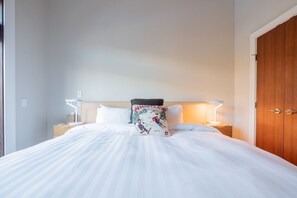 Ein ordentlich bezogenes Bett mit weißen Laken, einem Zierkissen und zwei Nachttischlampen auf einem Holznachttisch.