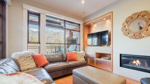Een moderne woonkamer met een leren bank, een flatscreen televisie, een open haard en grote ramen met uitzicht op de bergen.