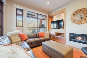 A modern living room with a leather sofa, a flat-screen TV, a fireplace, and large windows with a mountain view. - Luxury | AC | Private Hot Tub | BBQ | Pet friendly (Whistler)
