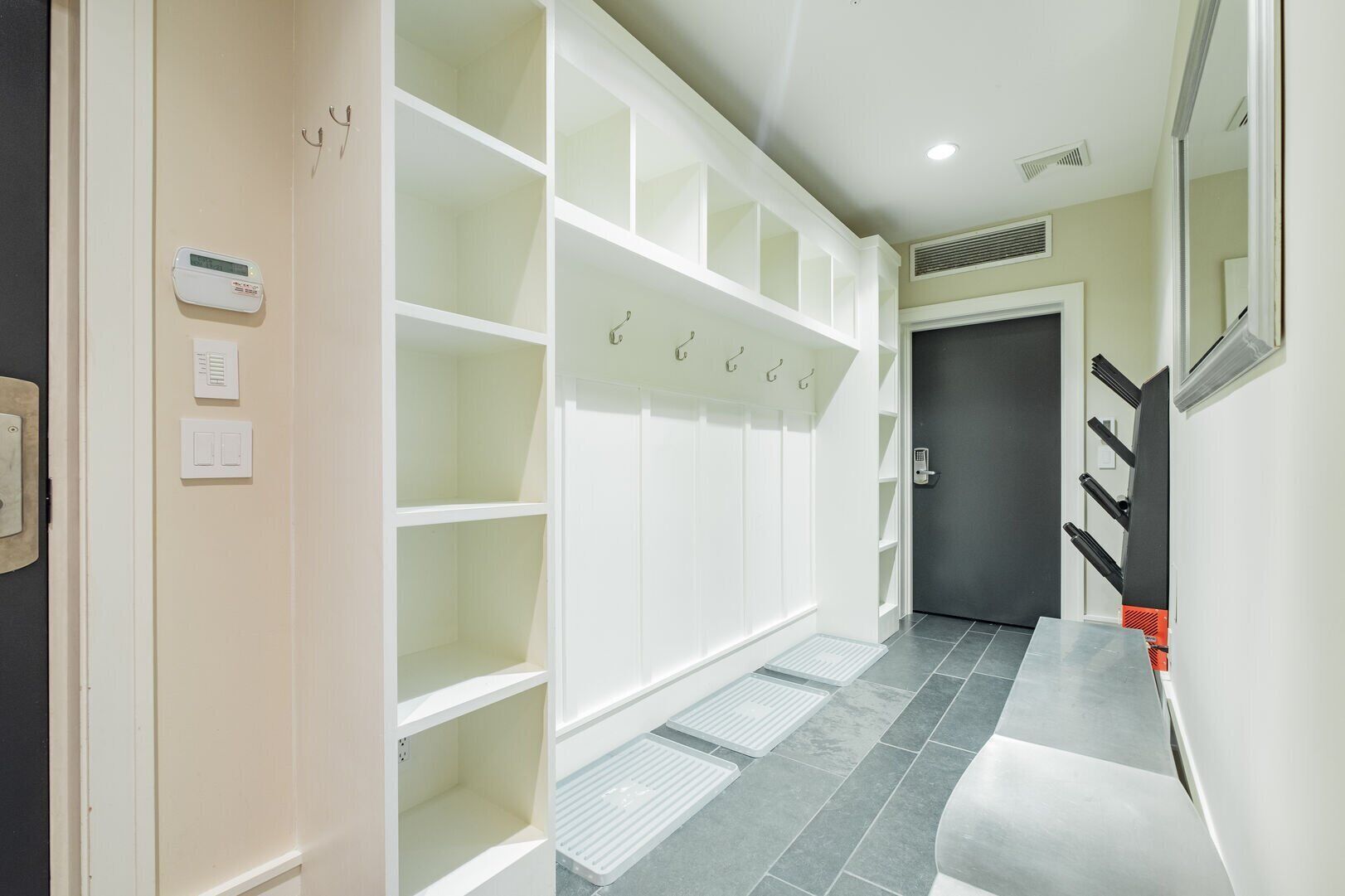 A hallway with white shelving units, a door, and a vent on the ceiling.