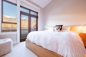Ein Schlafzimmer mit einem großen Bett, einem Nachttisch, einer Lampe und Bergblick durch eine Schiebetür.